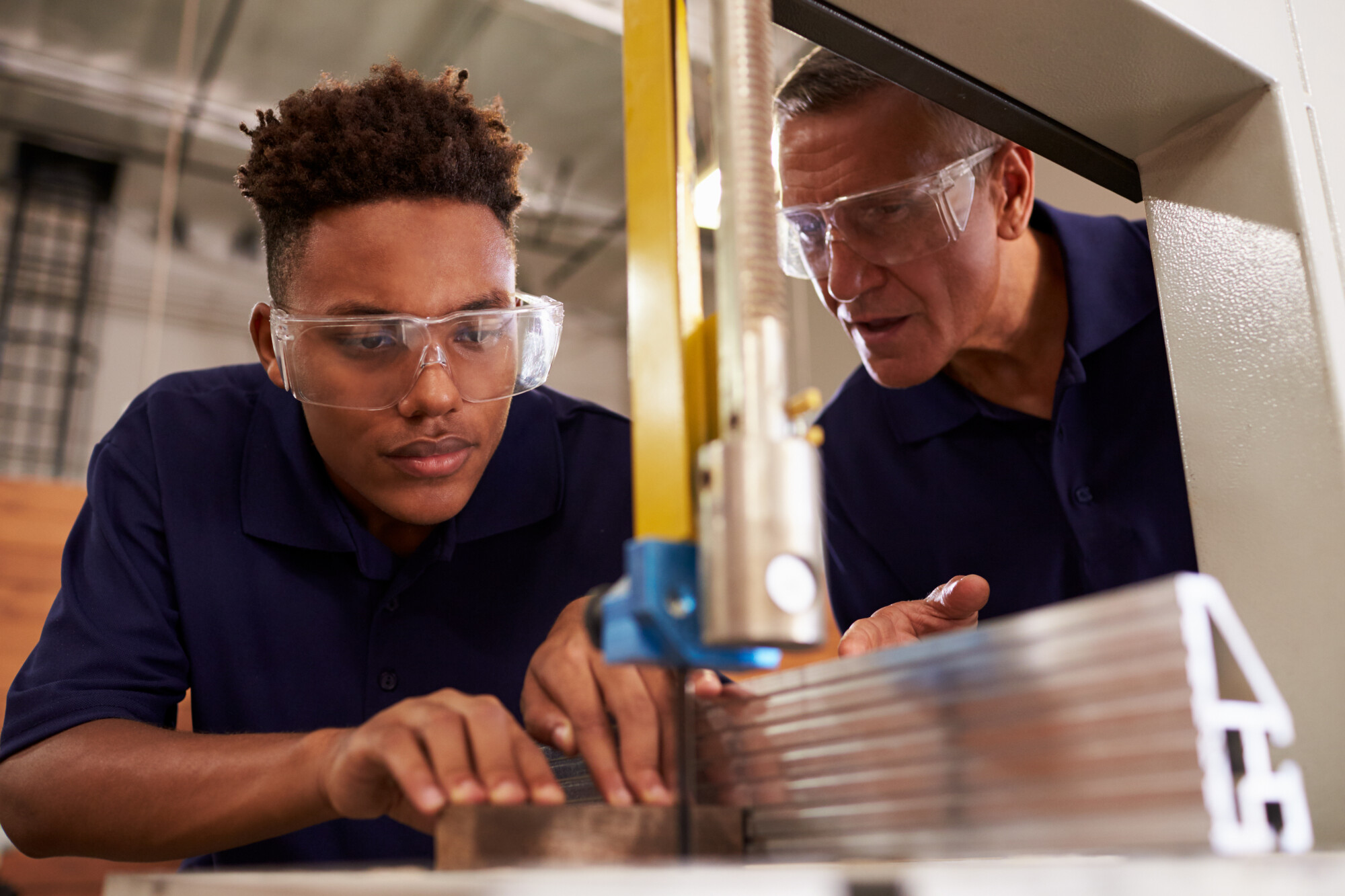 Teenager cutting metal with older man teaching
