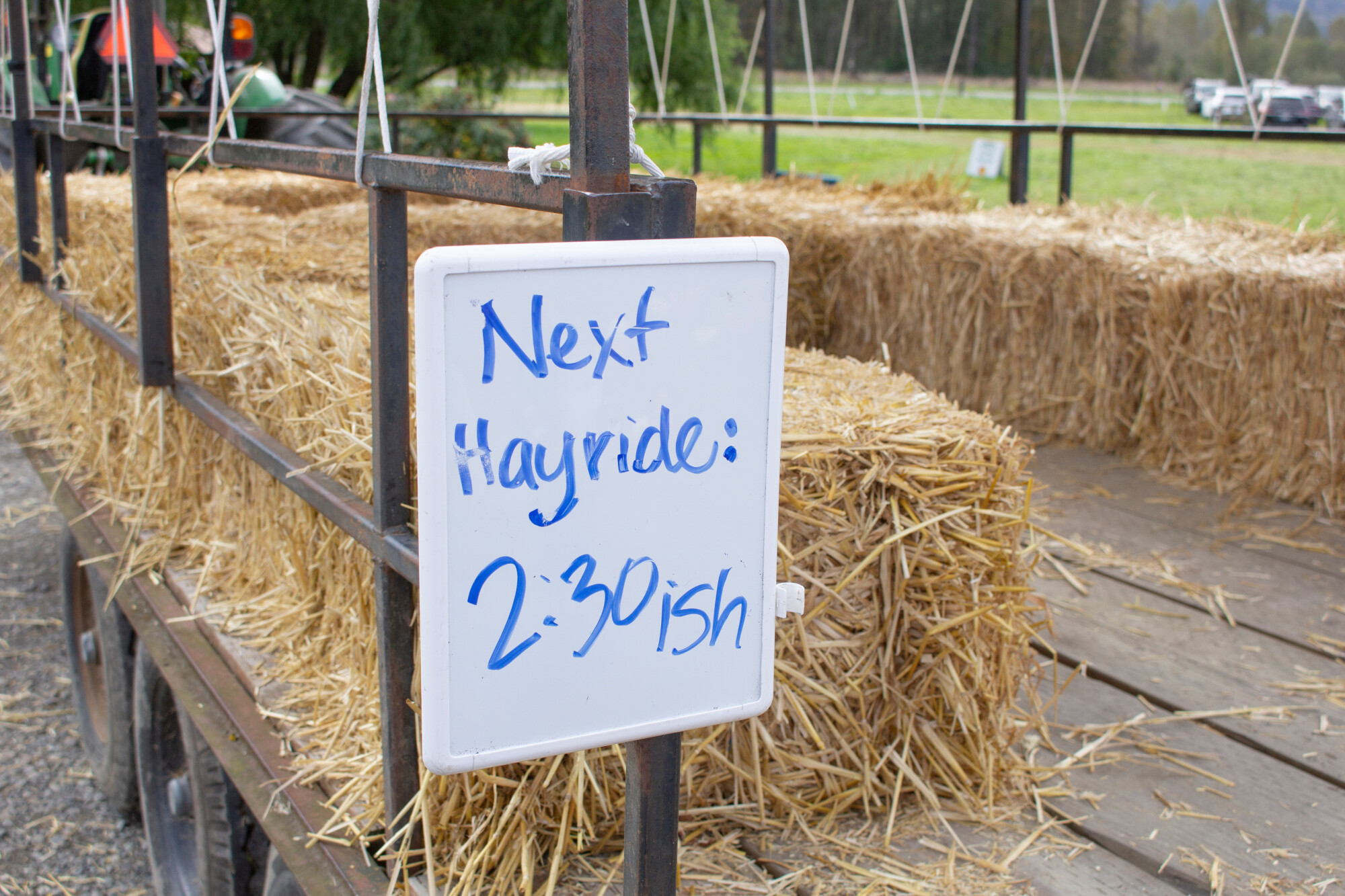 Riding cart with hay stacks as benches and whiteboard sign that reads "Next Hayride 2:30ish"