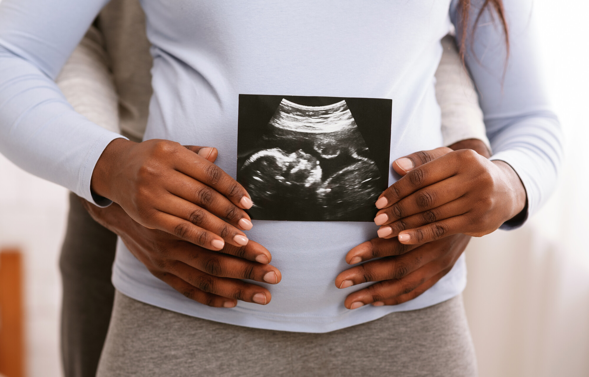 A man with his hands around the belly of a pregnant woman holding an ultrasound photo.