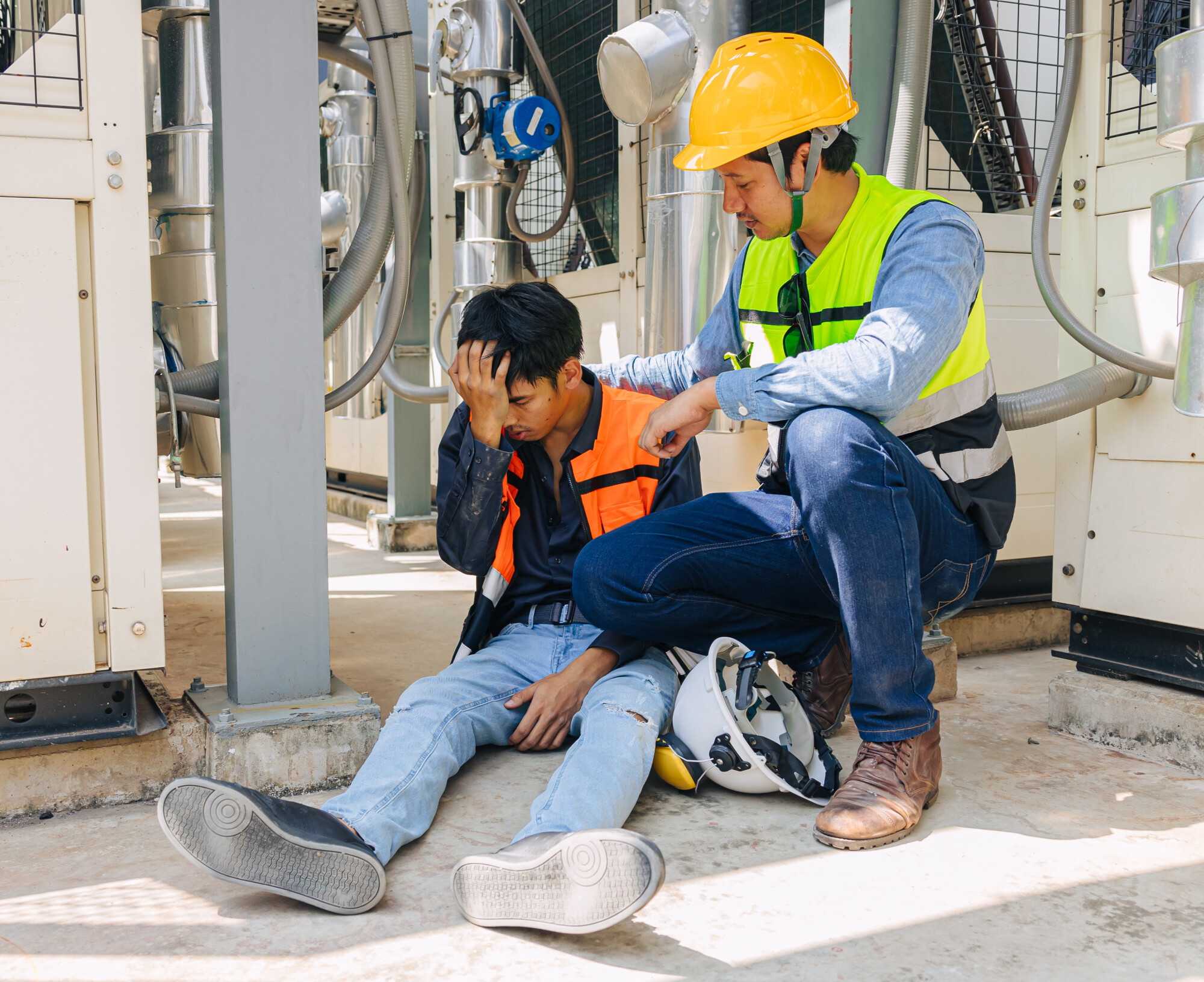 Man sitting on ground after fainting and another man comforting him