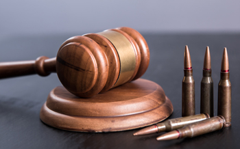 Wooden gavel laying against grey background with bullet casings standing straight up next to it
